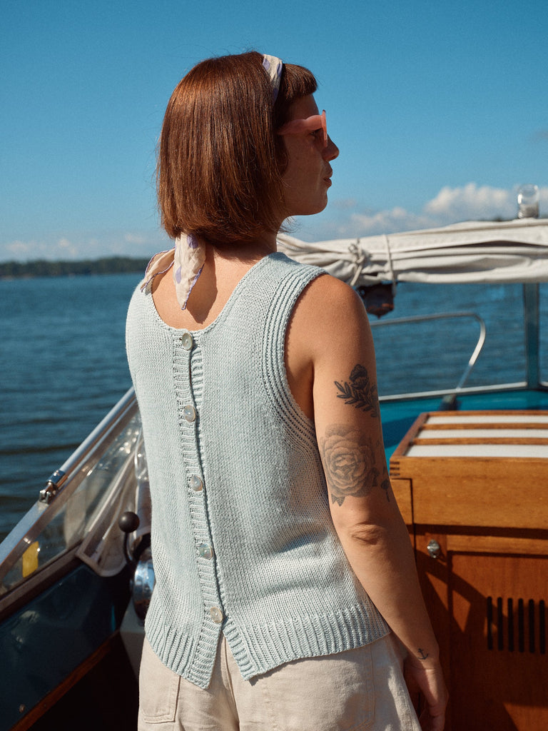 Laine Magazine 28 — chaleco gris con botones, de espaldas frente al mar