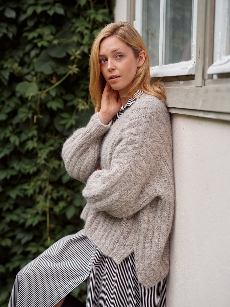 Laine Magazine 29 — cárdigan gris claro con textura, apoyada en un muro con hiedra